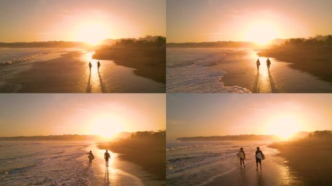 空中轮廓: 几个冲浪者在金色日出时沿着海滩散步