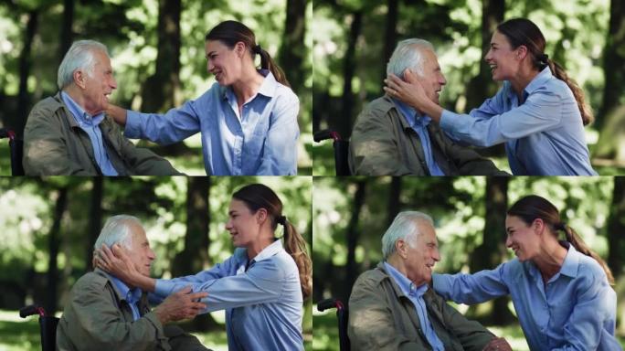 电影拍摄的快乐孙女在轮椅上给祖父以情感的吻，以此作为绿色公园中爱与尊重的标志。生活观念，祖父母，世代