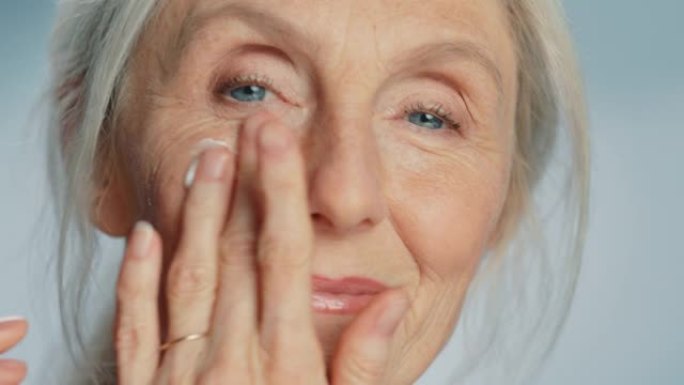 美丽的高级女人的特写肖像在眼霜下轻轻涂抹。老年女士用天然抗衰老化妆品使皮肤柔软、光滑、无皱纹。美容护