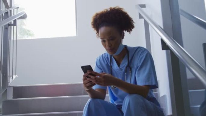 混血女医生戴着口罩坐在医院的楼梯上使用智能手机