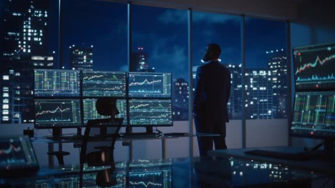 成功的商人在深夜向窗外望去。现代对冲基金办公室与计算机多显示器工作站实时股票，商品和交易所市场图表。