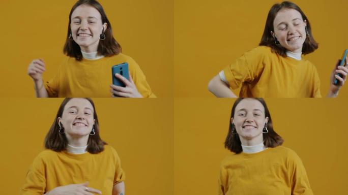 快乐女士戴着耳罩，拿着智能手机在黄色背景上跳舞的慢动作肖像