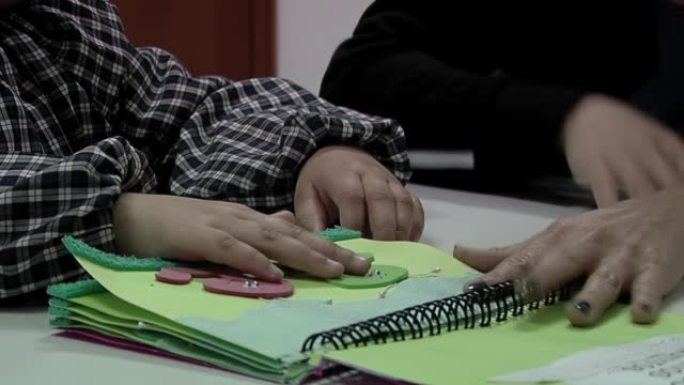 老师在阿根廷的一所公立学校为盲人和视障儿童提供帮助，帮助幼儿园的孩子阅读盲文字母。特写。