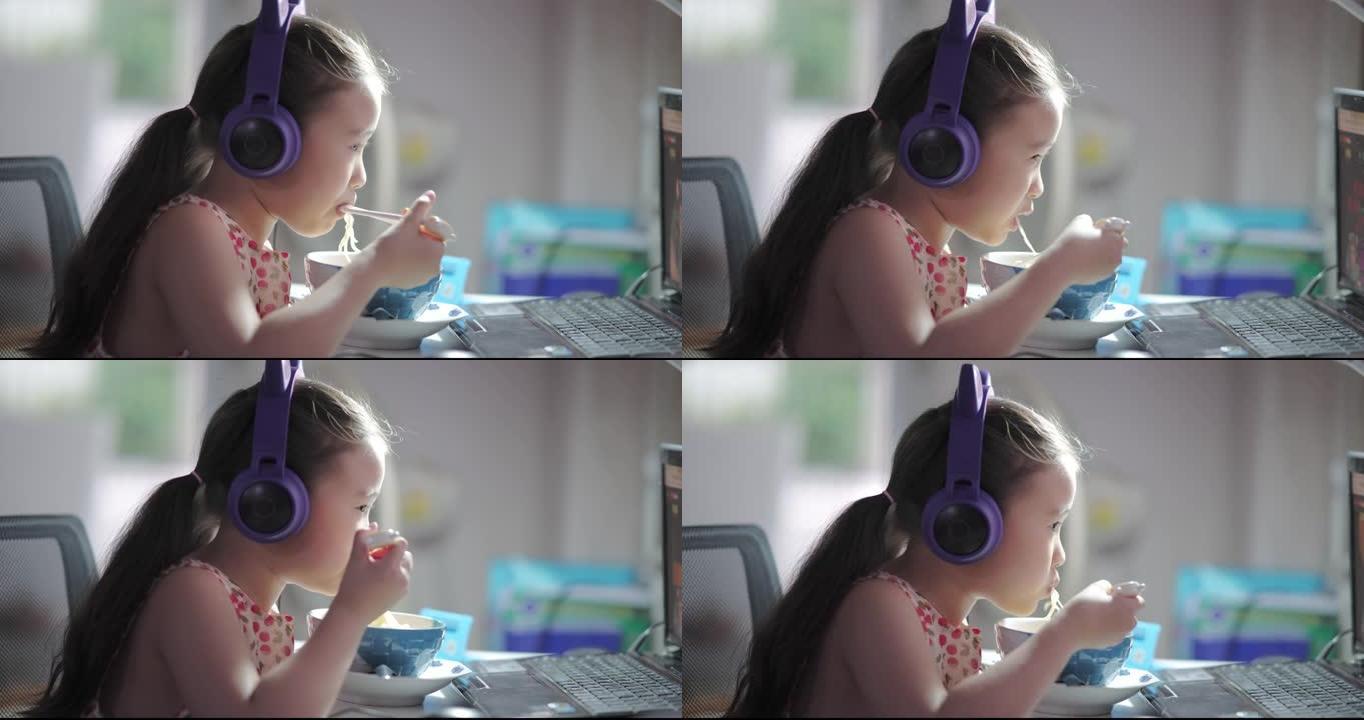在家在线上课期间，女孩在电脑屏幕前吃面