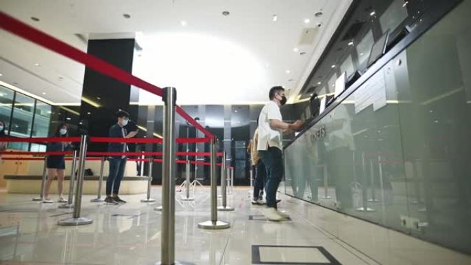 低角度的亚洲华人观众在售票柜台前排队购买电影票和爆米花饮料，在电影院放映前进行非接触式支付