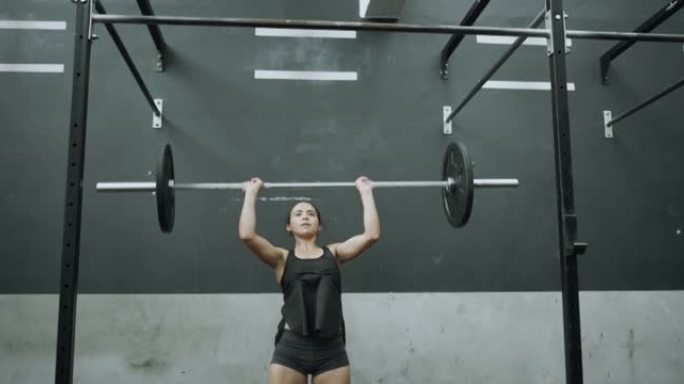 4k视频片段，一名年轻女子在健身房用杠铃进行头顶按压