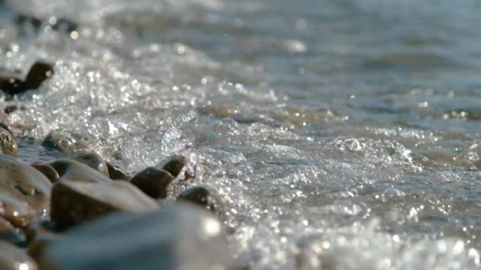 特写: 膨胀冲刷在空旷的海岸线上散落的圆形石头上。