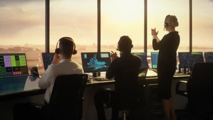 日落时在现代机场塔楼工作的多元化空中交通管制团队。管制员在装满计算机的房间里拍手庆祝新商用飞机的首次
