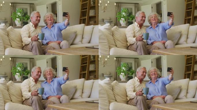 微笑的高加索高级夫妇从坐在家里沙发上的智能手机上自拍