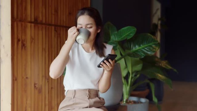 放松女人早上喝咖啡和智能手机。