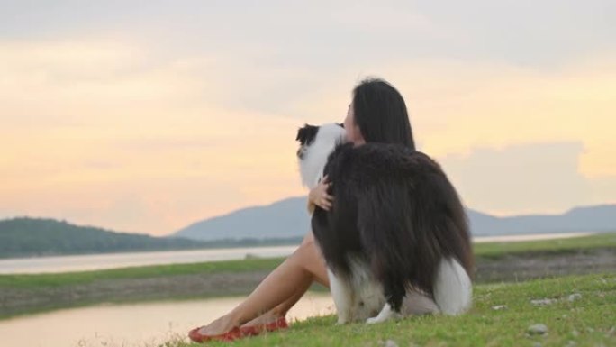 年轻的亚洲女孩和她的狗在自然公园享受美丽的夏日日落。