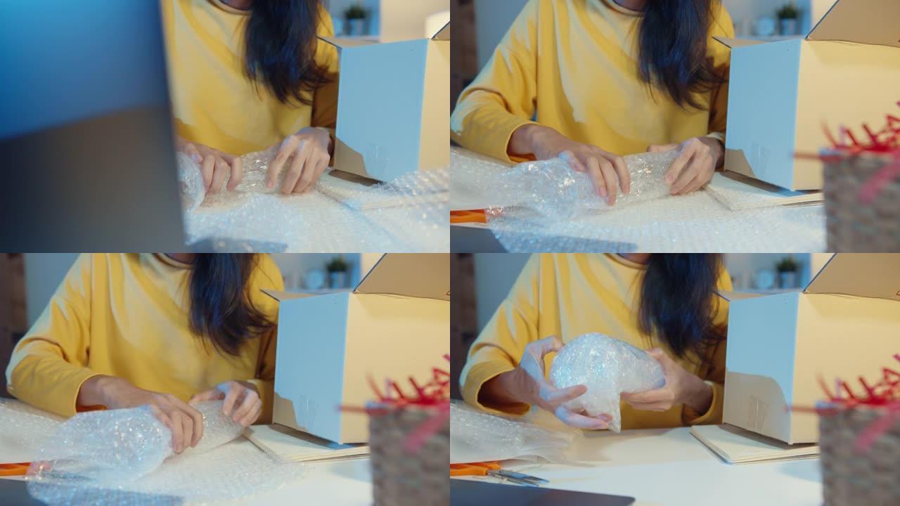 年轻的亚洲女商人包装玻璃使用气泡包装，晚上在家庭办公室支持损坏易碎产品。