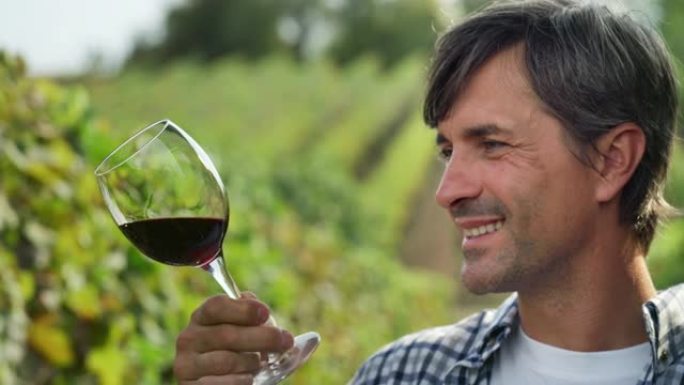 中年男子在葡萄园闻到和品尝红酒的肖像。专业男性农民和酿酒师享受工作成果和酒庄产品质量的真实照片