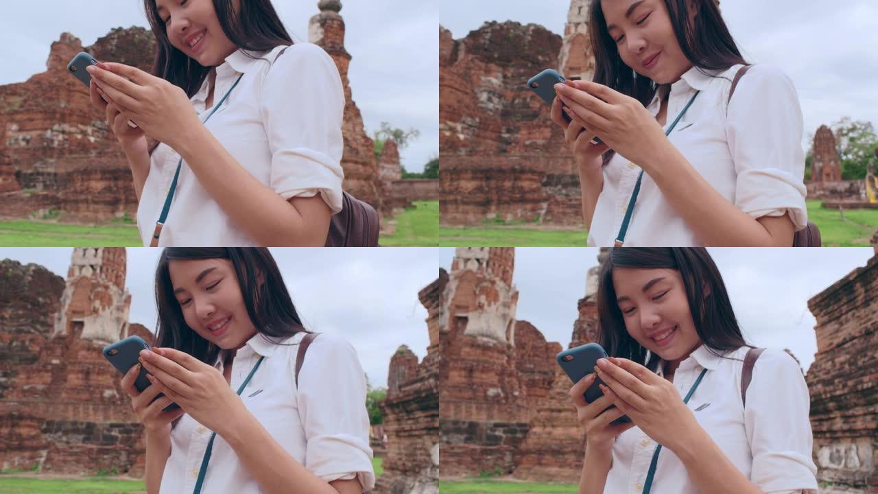 开朗美丽的年轻亚洲背包客博主女人休闲与相机看照片智能手机微笑与快乐的脸旅行宝塔在老城。