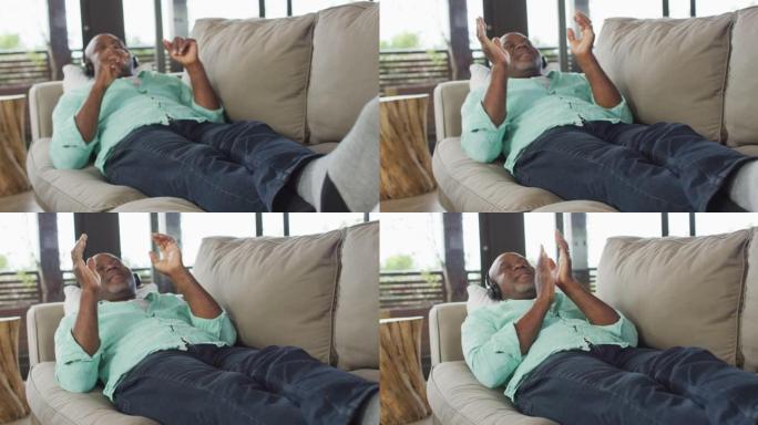 快乐的非洲裔美国老人放松，躺在沙发上戴着耳机听音乐