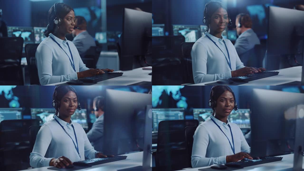 欢乐美丽的技术客户支持专家在呼叫中心控制室的计算机上工作时正在耳机上交谈，该控制室充满了同事，显示屏