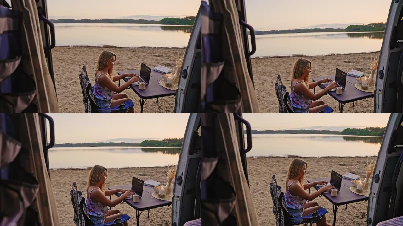 在海滩上日落时，深色头发的女性在笔记本电脑上工作，旁边是一辆野营车