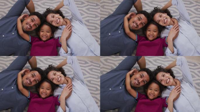 快乐的西班牙裔父母和女儿拥抱躺在客厅的地板上