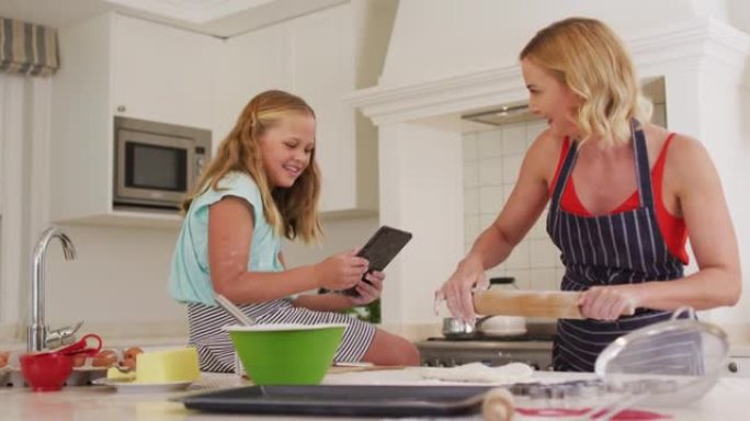 高加索母亲和女儿使用数字平板电脑并在家里的厨房里一起烘烤