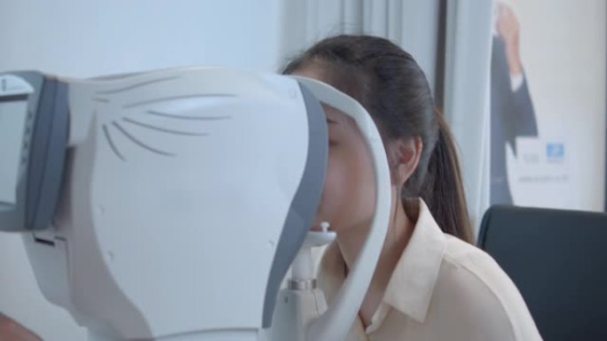 年轻的亚洲妇女在光学商店用医疗机器进行眼睛测试