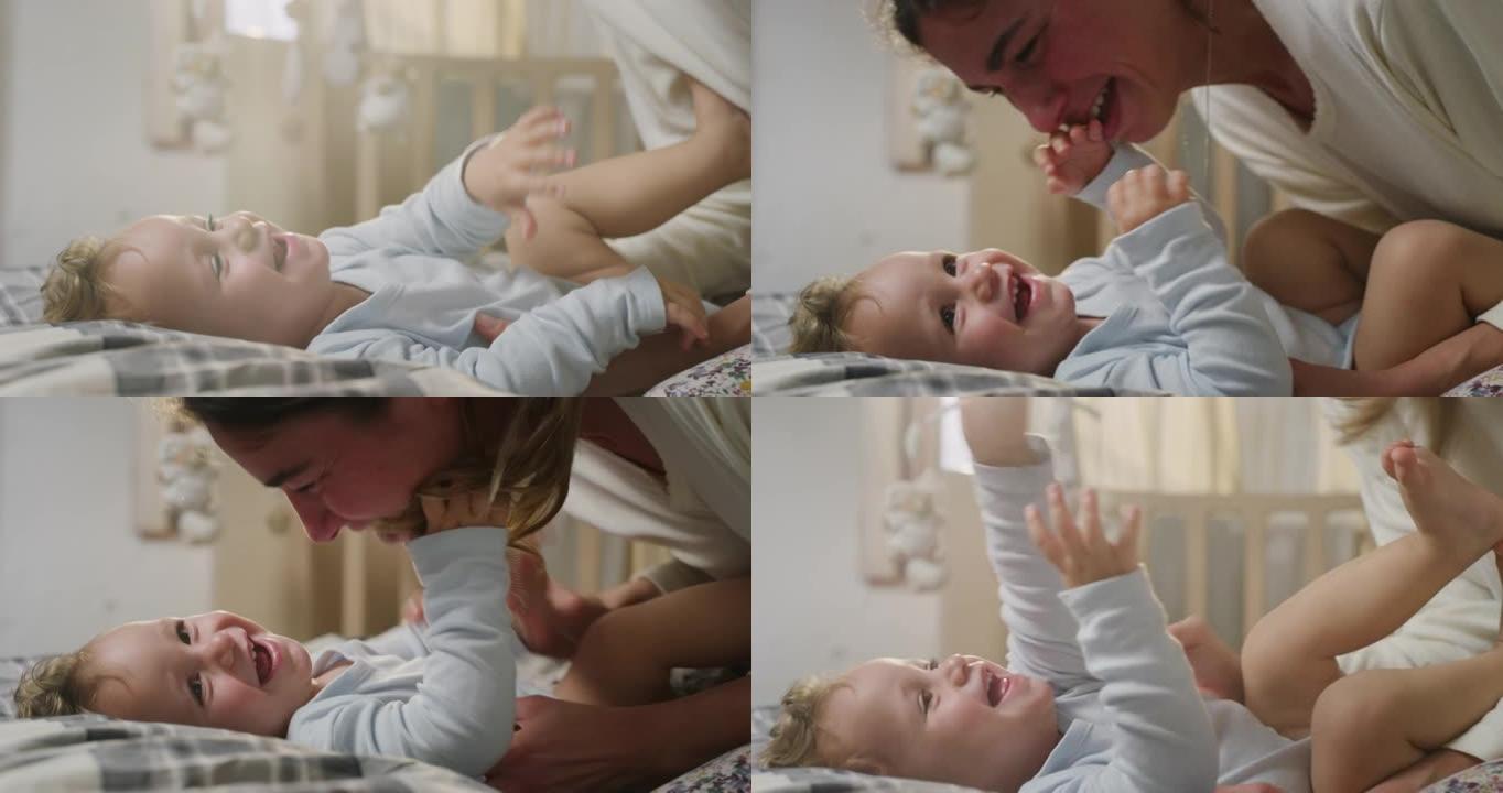 年轻快乐的母亲的电影特写镜头正在挠痒痒，并与她蹒跚学步的男婴在一个早晨醒来的托儿所里玩耍。爱的概念，