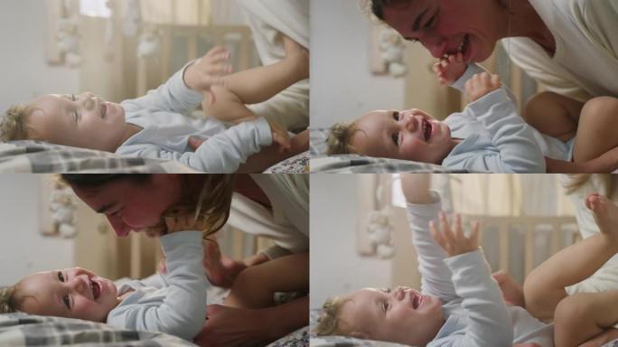 年轻快乐的母亲的电影特写镜头正在挠痒痒，并与她蹒跚学步的男婴在一个早晨醒来的托儿所里玩耍。爱的概念，