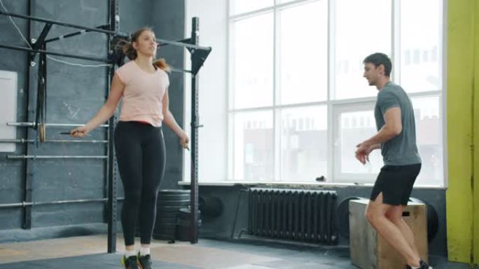 跳绳跳跳的年轻女孩和男人在健身房激励女人的肖像