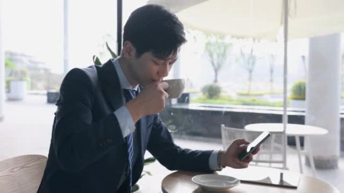 亚洲商人使用电话并在咖啡馆喝咖啡