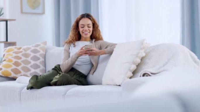一个放松的女人在电话上阅读和回复有趣的文字。一位女士在沙发上玩在线手机游戏。笑女性聊天或在社交媒体上