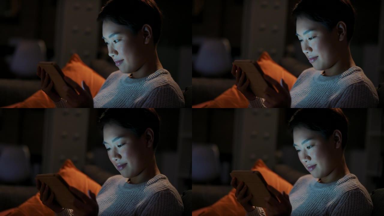 一名年轻女子在夜间在家中在沙发上使用数字平板电脑的4k视频片段