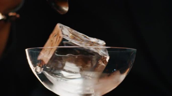 调酒师的特写镜头是将专业的水晶冰块放入玻璃杯中，同时在酒吧或迪斯科俱乐部为顾客准备酒精鸡尾酒。