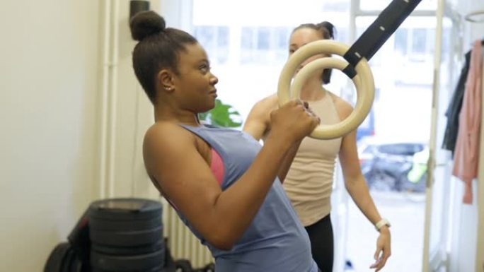 健康的女人和她的私人教练一起做体操戒指锻炼