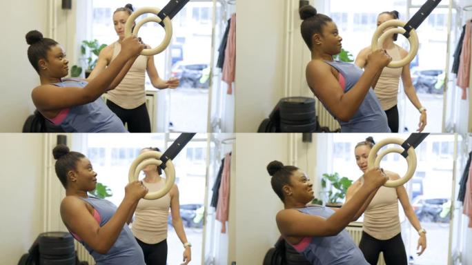 健康的女人和她的私人教练一起做体操戒指锻炼
