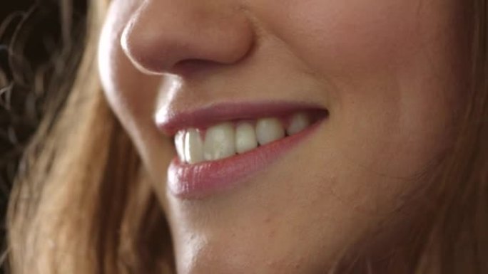 微笑女人的嘴唇和露出牙齿的特写镜头，同时穿着粉红色的口红，化妆和化妆品。爆头，脸部和嘴巴的美丽微笑细