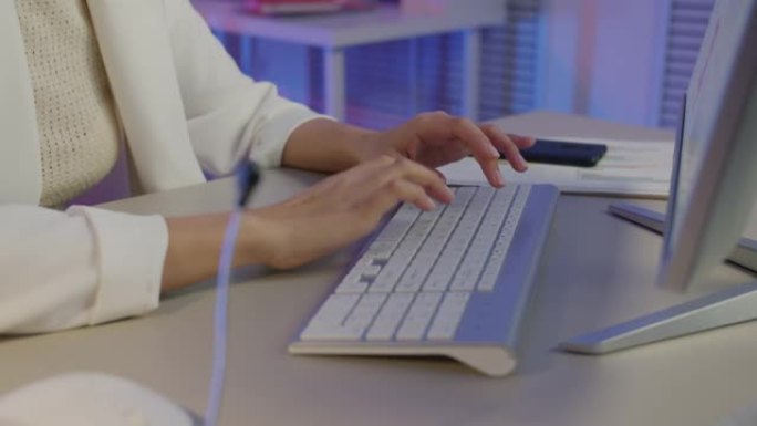 在黑暗的办公室中使用PC键盘打字的女性手的特写