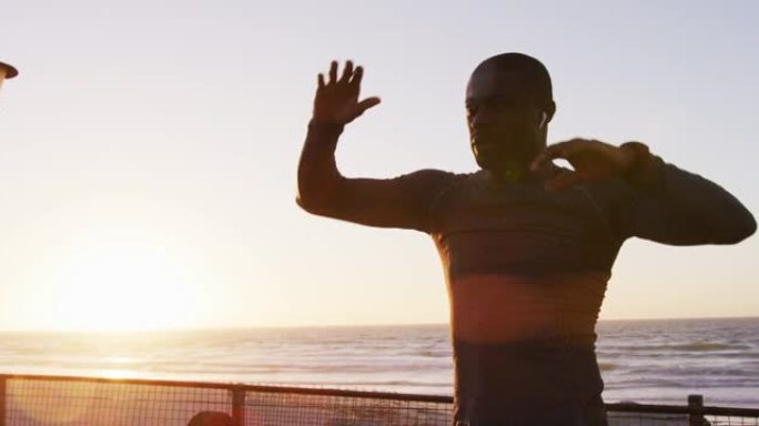 专注的非洲裔美国男子伸展运动，在日落时在海边户外运动