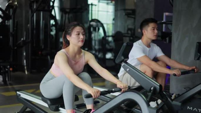 年轻男女在健身房用划船机锻炼