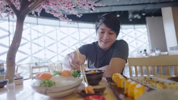 亚洲男子高兴地在桌上吃鲑鱼生鱼片和各种日本食物。