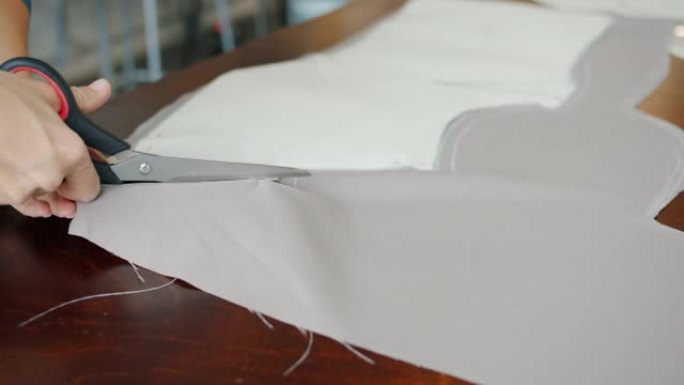 裁缝在餐桌上工作时，女性双手用剪刀切割织物的特写镜头