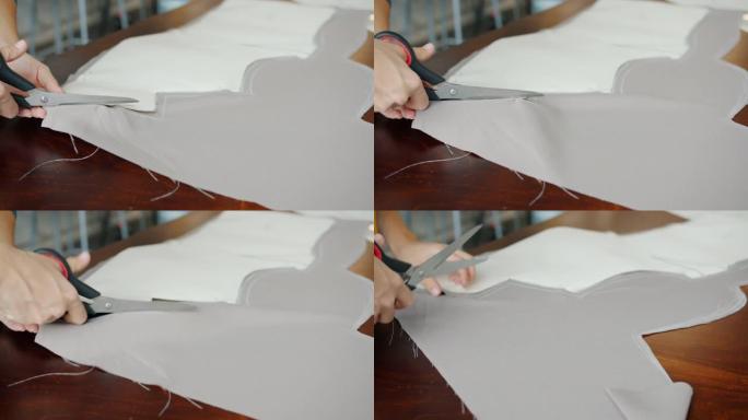 裁缝在餐桌上工作时，女性双手用剪刀切割织物的特写镜头