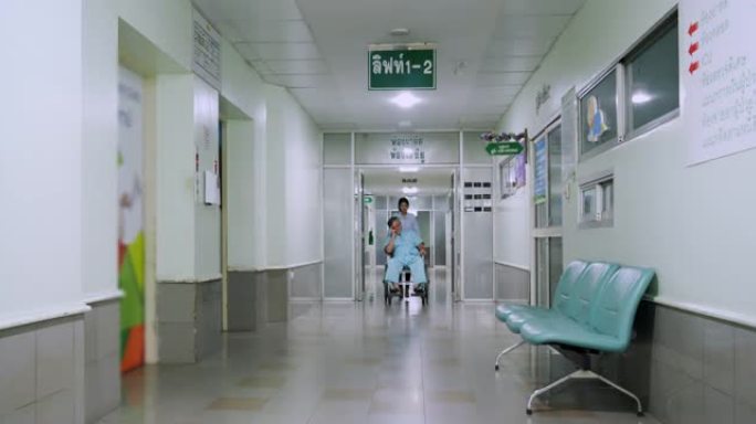 后视图，医生和护士在现代医院大楼的医院走廊中行走，而助理推动亚洲高级男性患者坐在轮椅上。医院概念。