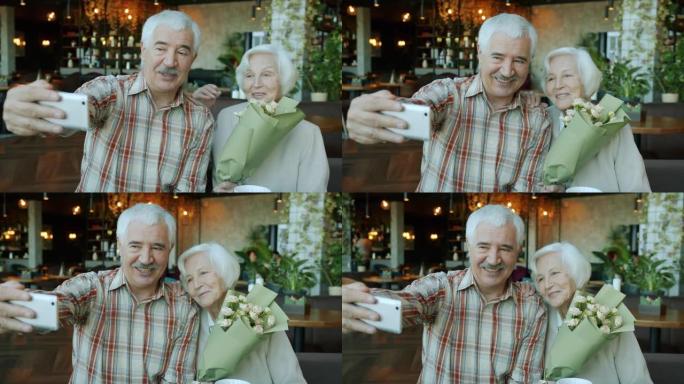 高级丈夫和妻子使用智能手机在餐厅拍照，而女人拿着鲜花