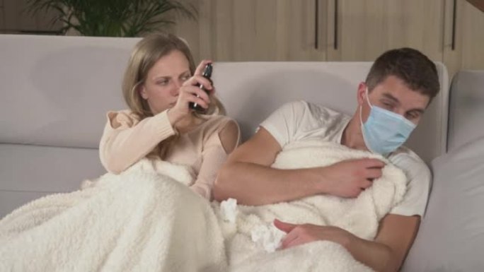 特写。两人在电视上盖着毯子，而患有流感的人打喷嚏