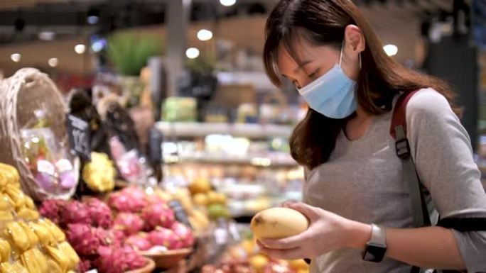 戴着医用口罩的年轻亚洲妇女在超市里用杂货店推车走路