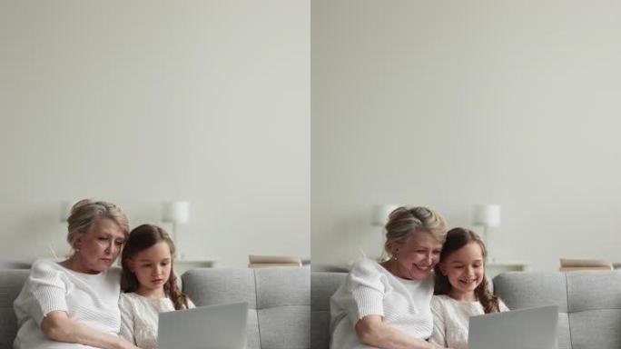 可爱的奶奶她的孙女坐在沙发上，配有无线电脑