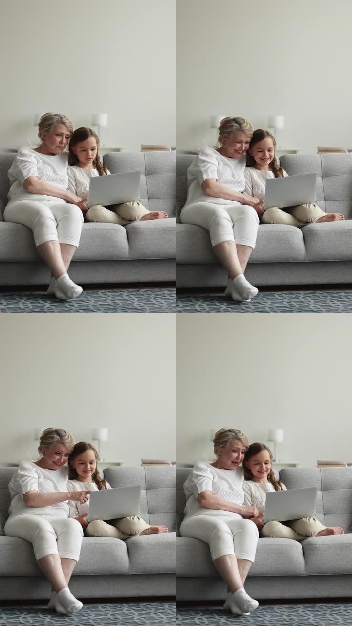 可爱的奶奶她的孙女坐在沙发上，配有无线电脑