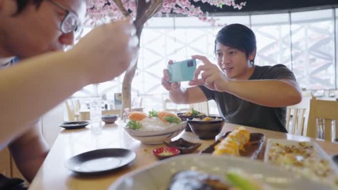 亚洲男子在日本餐厅拍摄他的朋友吃寿司卷