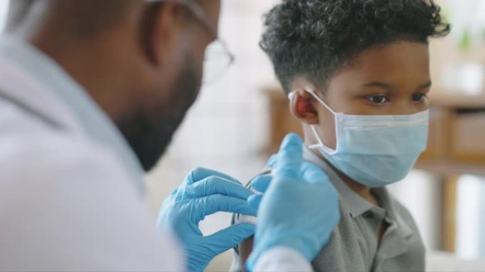 非裔美国人的男性医生或护士在医院或家庭为9岁儿童的肩膀注射疫苗或疫苗，并一起接种疫苗和预防冠状病毒大