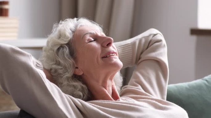 退休的成熟白衣女人在舒适的沙发上做白日梦。