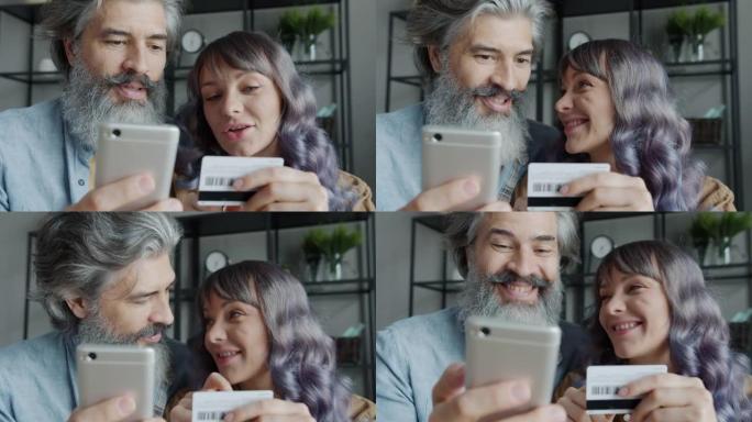 快乐的夫妻在网上购物，用信用卡和智能手机在家室内大笑